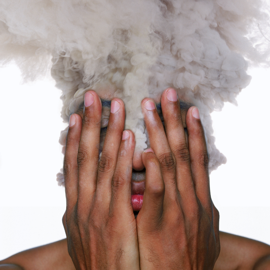 Stress damages this man's skin as he holds his face in his hands while smoke billows from his head.