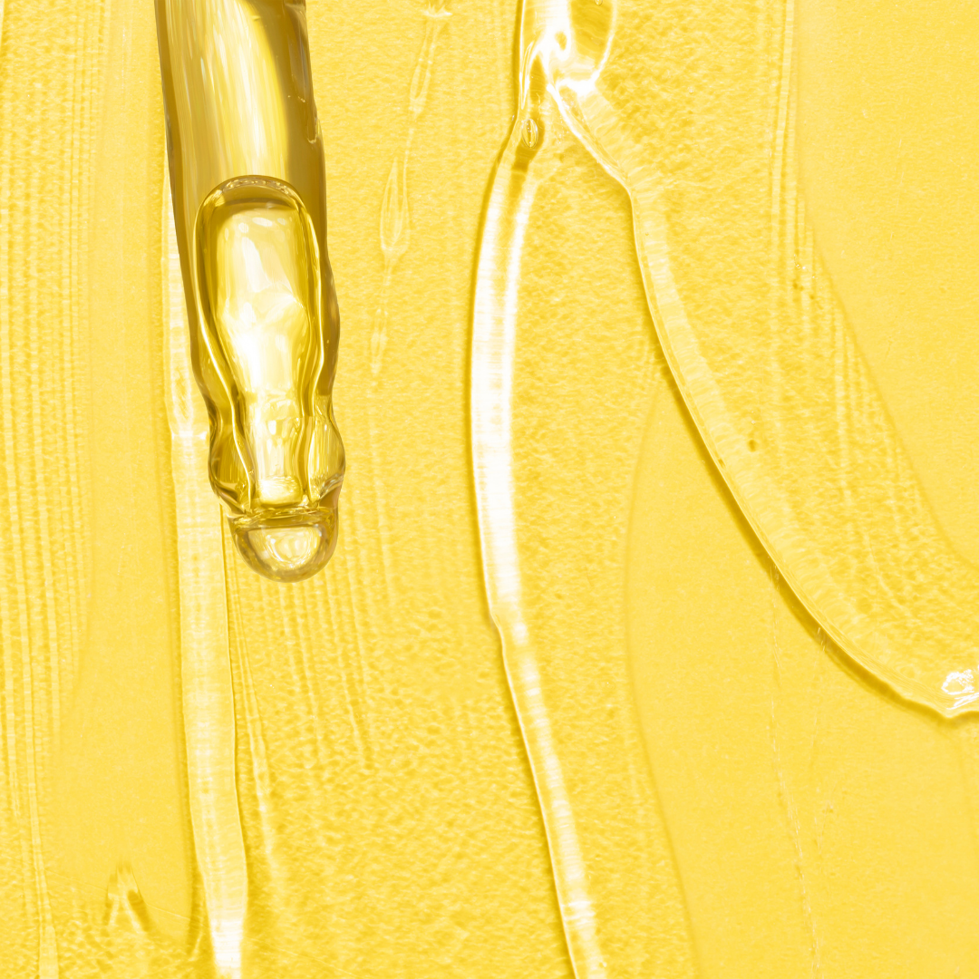 Yellow background with drops and smears of clear viscous retinol gel showcasing the texture of anti-aging skincare serum