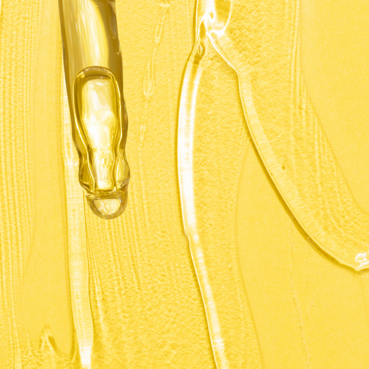 Yellow background with drops and smears of clear viscous retinol gel showcasing the texture of anti-aging skincare serum